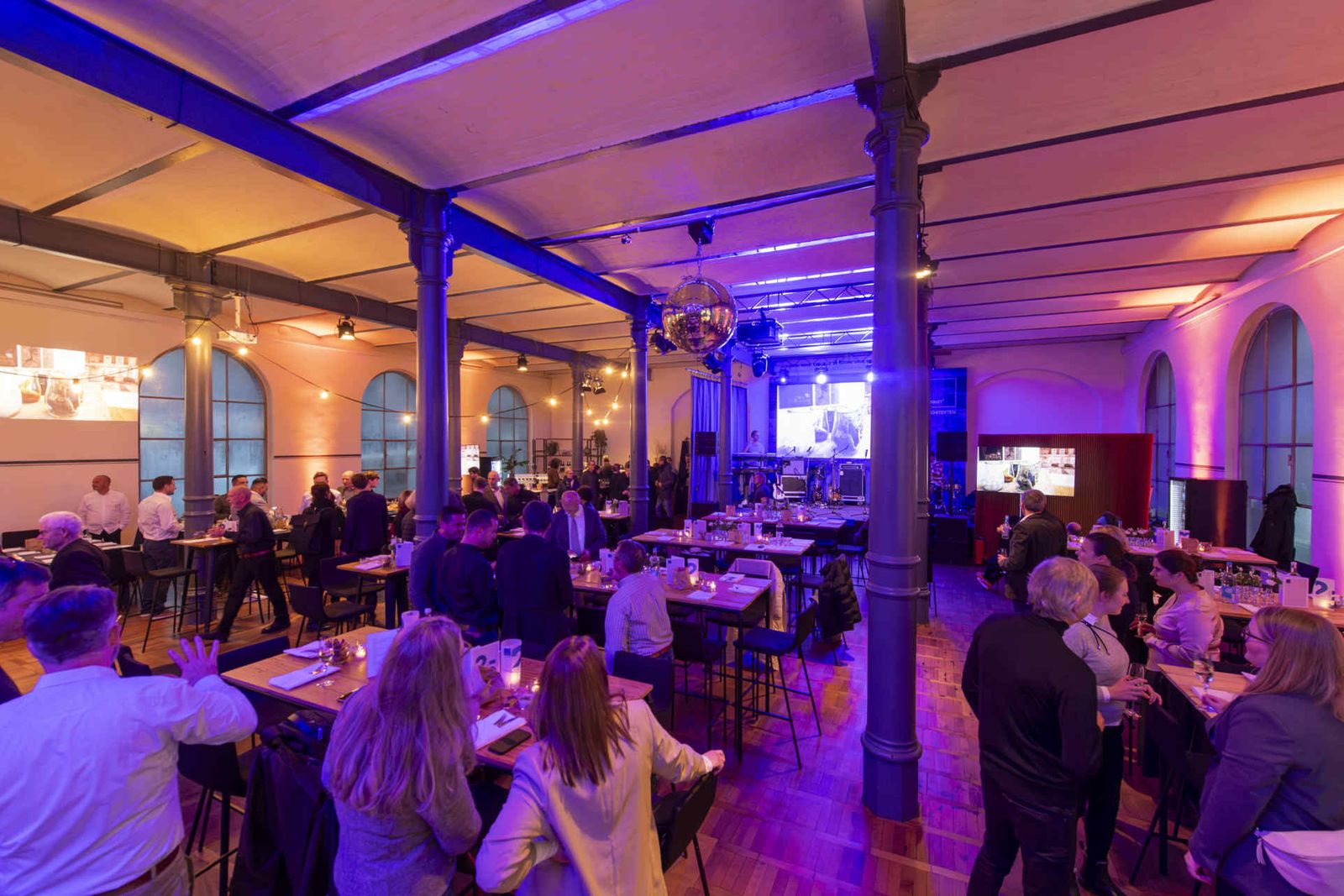 Eventsaal mit atmosphärischer Beleuchtung und Menschen während einer Veranstaltung.