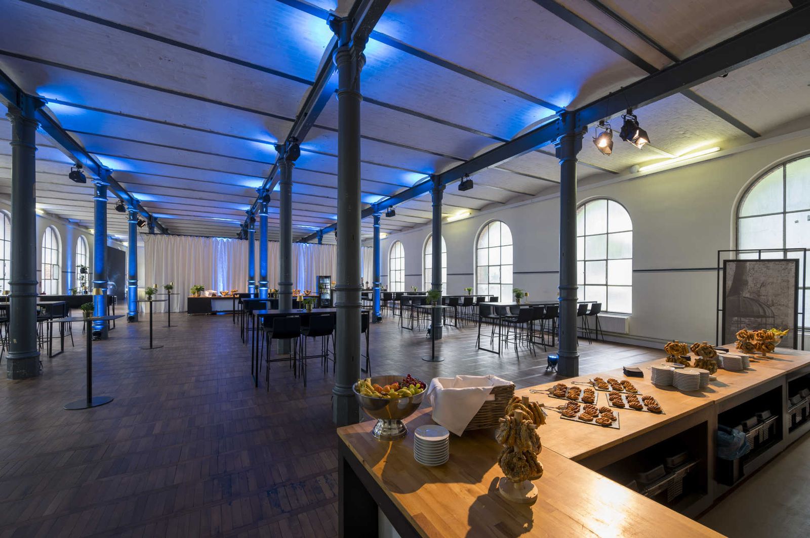 Großer Saal mit Holzboden, Säulen und Catering Station und Stehtischbrücken