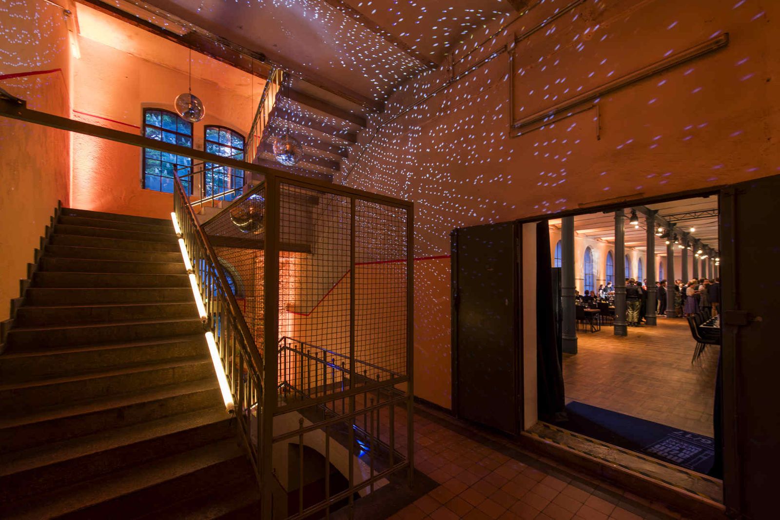 Treppenhaus mit atmosphärischer Beleuchtung und Blick in den Saal