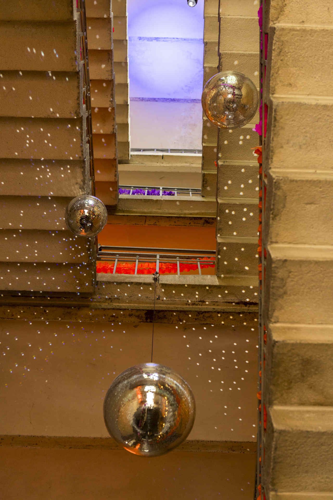 Blick in die Höhe eines Treppenhauses, dekoriert mit mehreren Discokugeln und bunten Girlanden