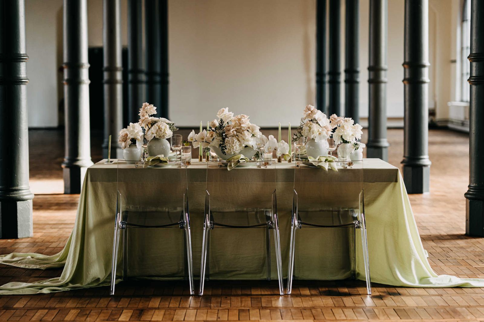 Festlich gedeckter Tisch mit grüner Tischdecke im Saal mit vielen Säulen und Holzparkett.