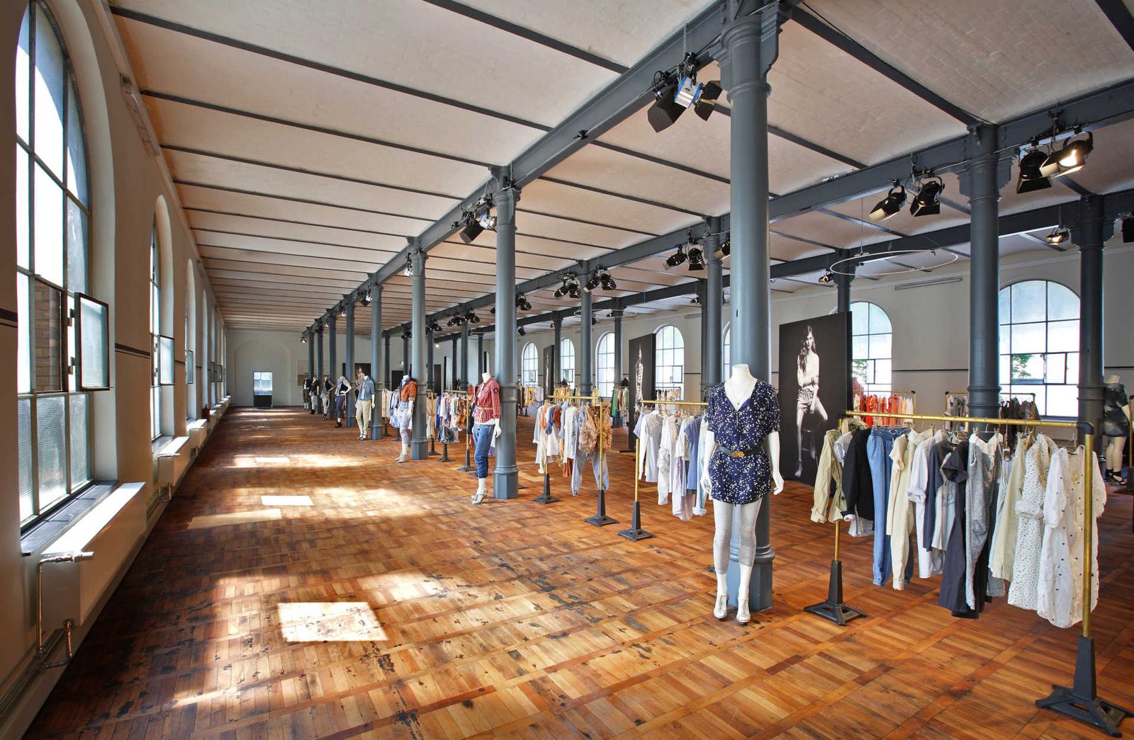 Long industrial hall with many clothing racks, mannequins and large posters.