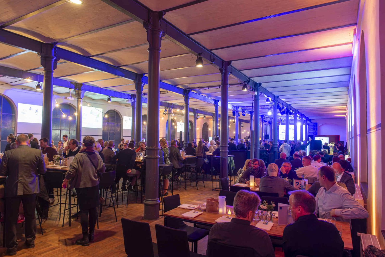Eventsaal mit atmosphärischer Beleuchtung und Menschen während einer Veranstaltung.