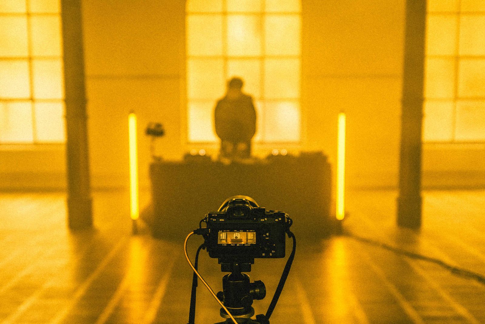 Kamera vor DJ am Pult mit Neon Röhren in großem Saal mit gelben Nebel