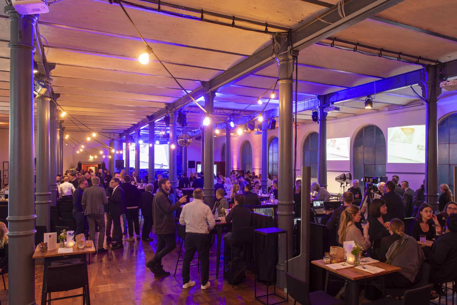 Eventsaal mit atmosphärischer Beleuchtung und Menschen während einer Veranstaltung.
