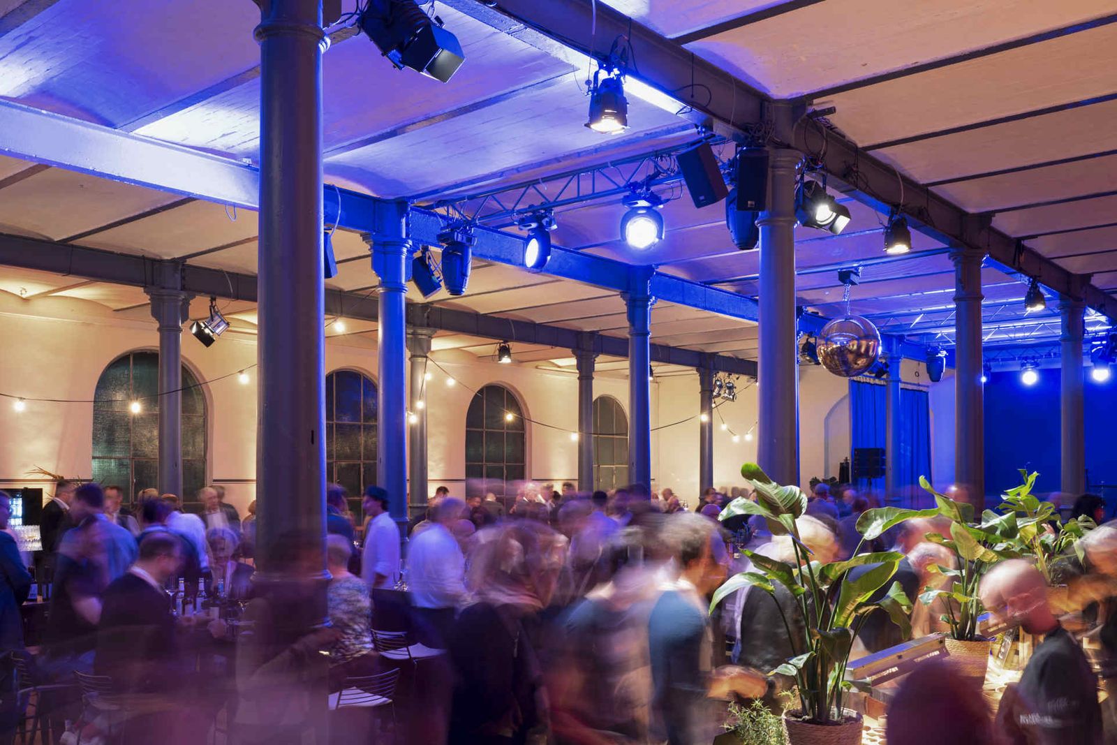 Eventsaal mit atmosphärischer Beleuchtung und Menschen während einer Veranstaltung.