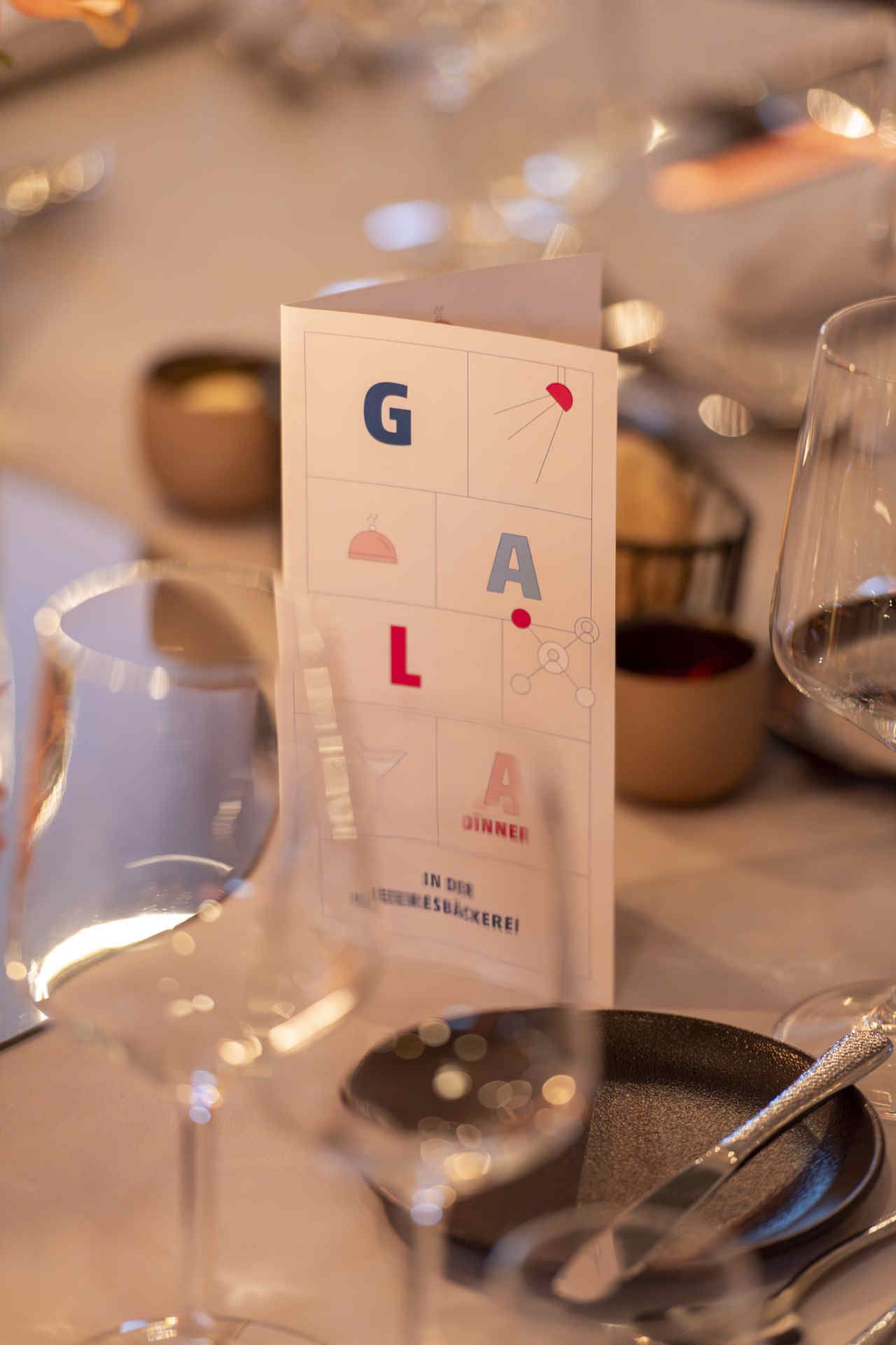 Auf gedecktem Tisch eine aufgestellte Karte mit der bunten Aufschrift: GALA