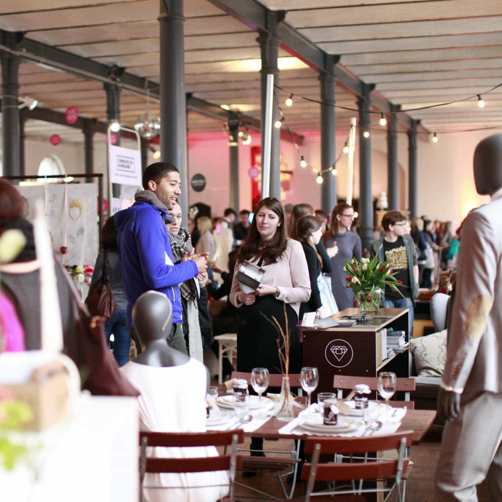 Helmchen Event + Location Magazin Heeresbäckerei Product Exhibition Several people standing in a large room with a set table in front of them
