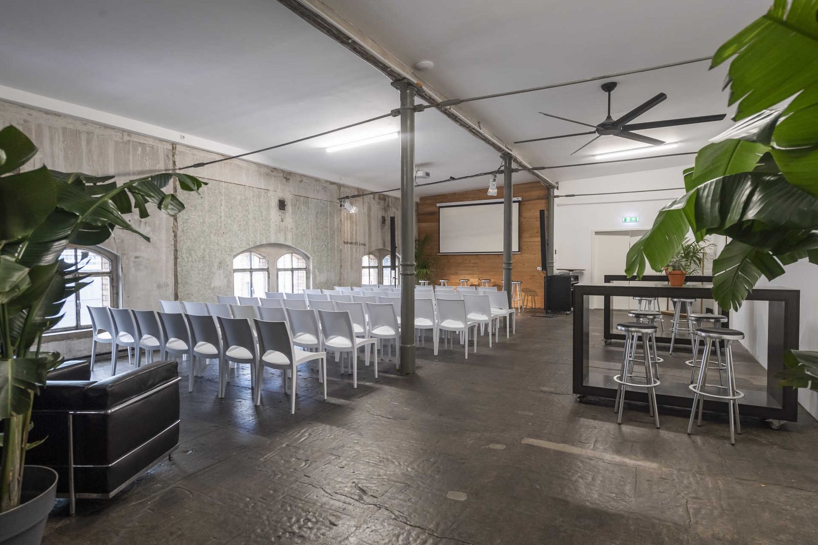 Industrielle Loftetage mit Konferenzbestuhlung und Leinwand vor Holzwand