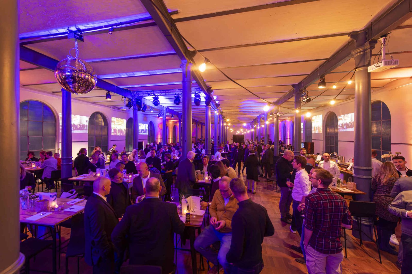 Eventsaal mit atmosphärischer Beleuchtung und Menschen während einer Veranstaltung.