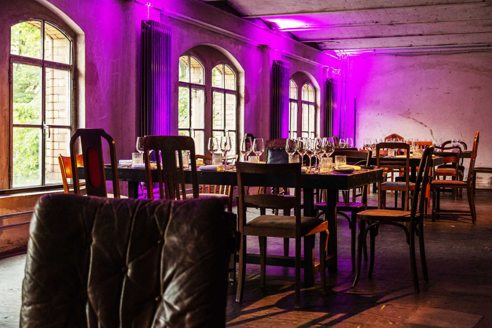 Gedeckte Holztische mit vintage Bestuhlung in pink erleuchtetem Loft mit Säulen.