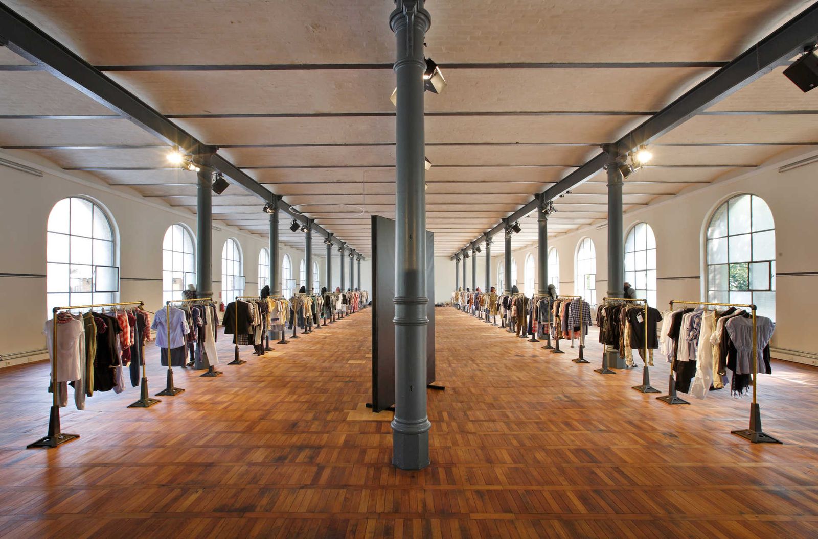 Industrial hall with columns and wooden parquet flooring with two long rows of clothing racks.
