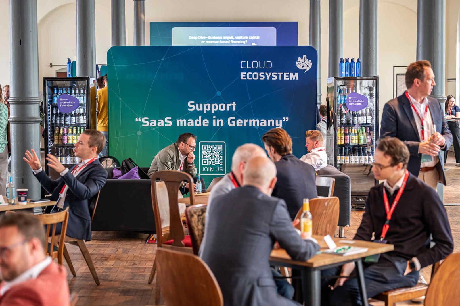 Helmchen Event + Location Magazin Heeresbäckerei Konferenz Tagung - Eventlocation mit Pressewand, Tischgruppen an denen Besucher sitzen und Selbstbedienungskühlschränke