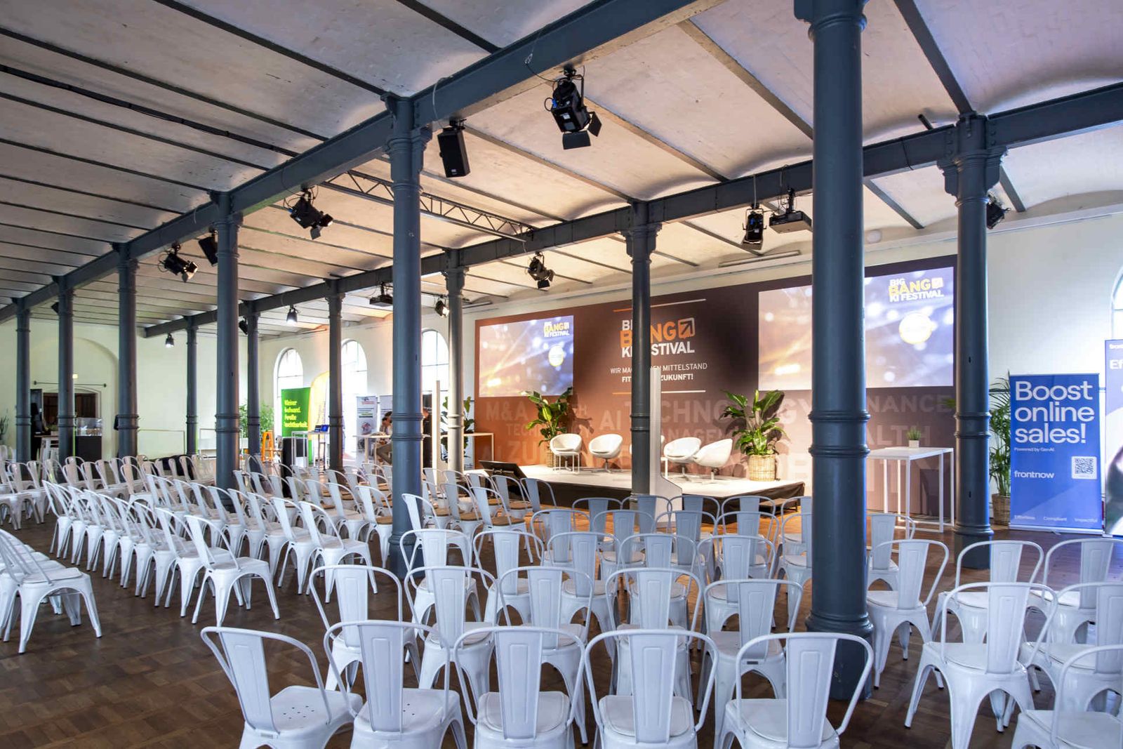 Großer Saal mit Reihenbestuhlung und einer Bühne mit großem Backdrop und Leinwänden
