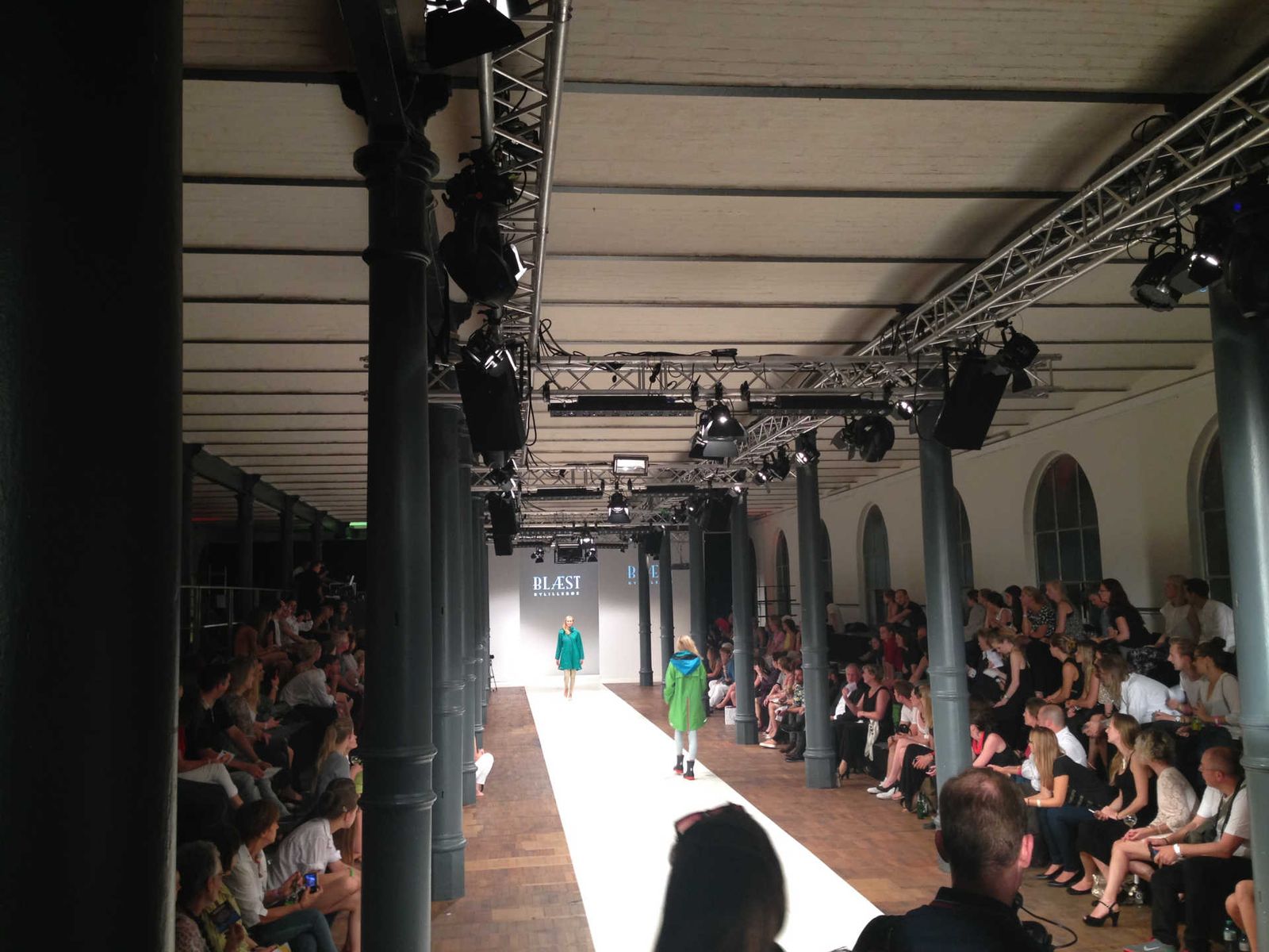 Black and white photo of fashion show with model at the end of the runway.