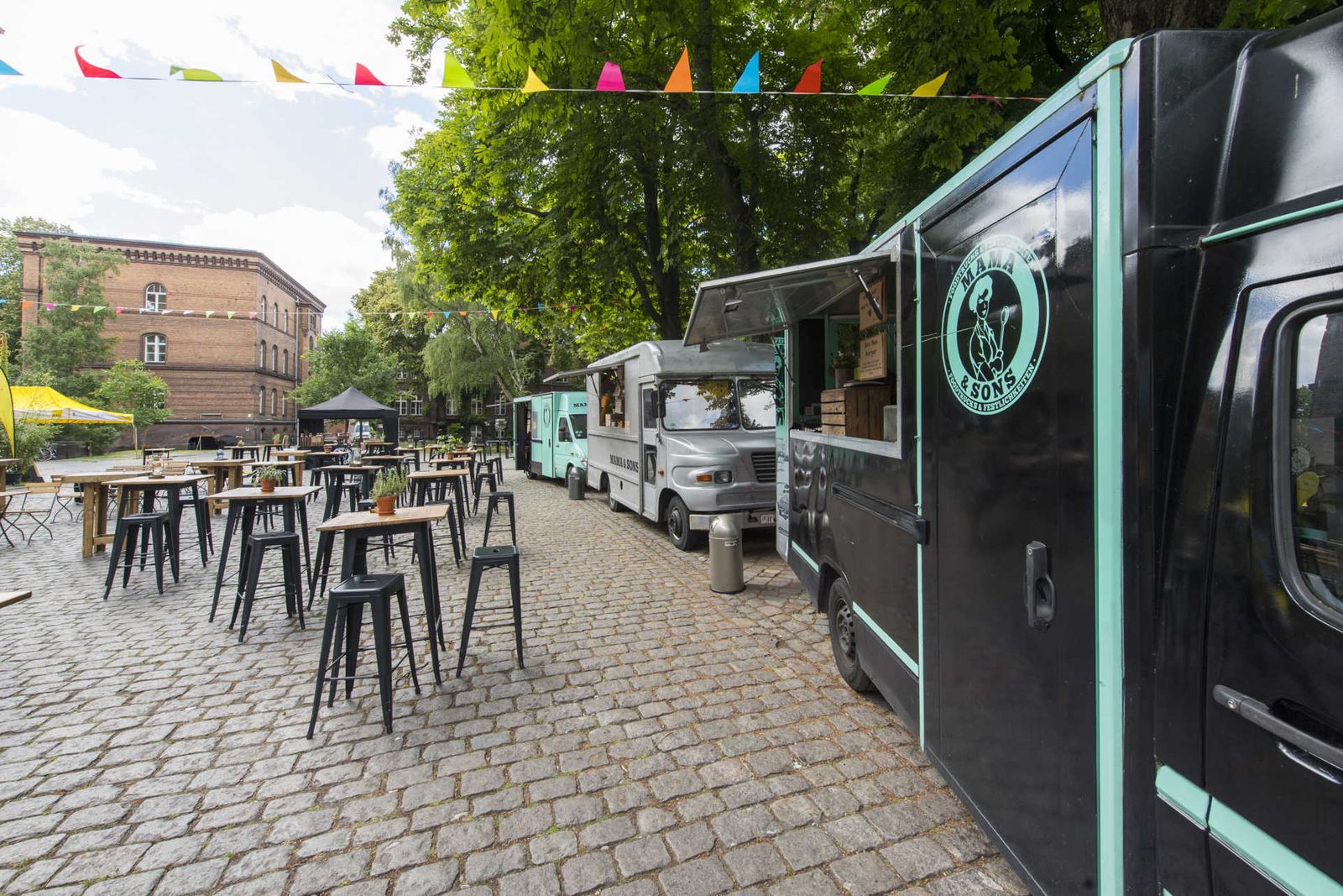 Außenbereich mit drei Foodtrucks und Outdoor Mobiliar und Wimpelkette.