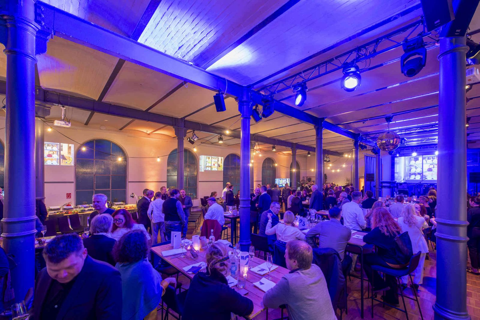 Eventsaal mit atmosphärischer Beleuchtung und Menschen während einer Veranstaltung.