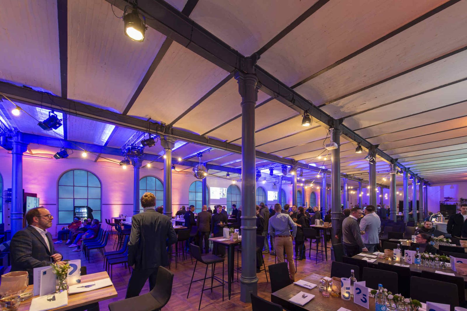Eventsaal mit atmosphärischer Beleuchtung und Menschen während einer Veranstaltung.