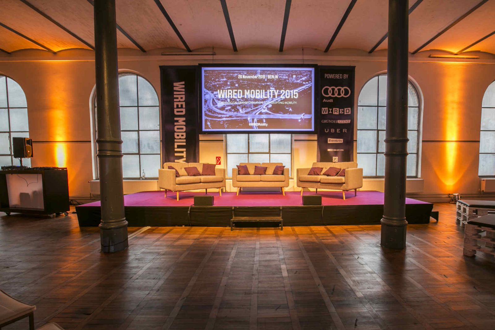 Blick auf eine Bühne mit lila Teppich, 3 Sofas und Leinwand