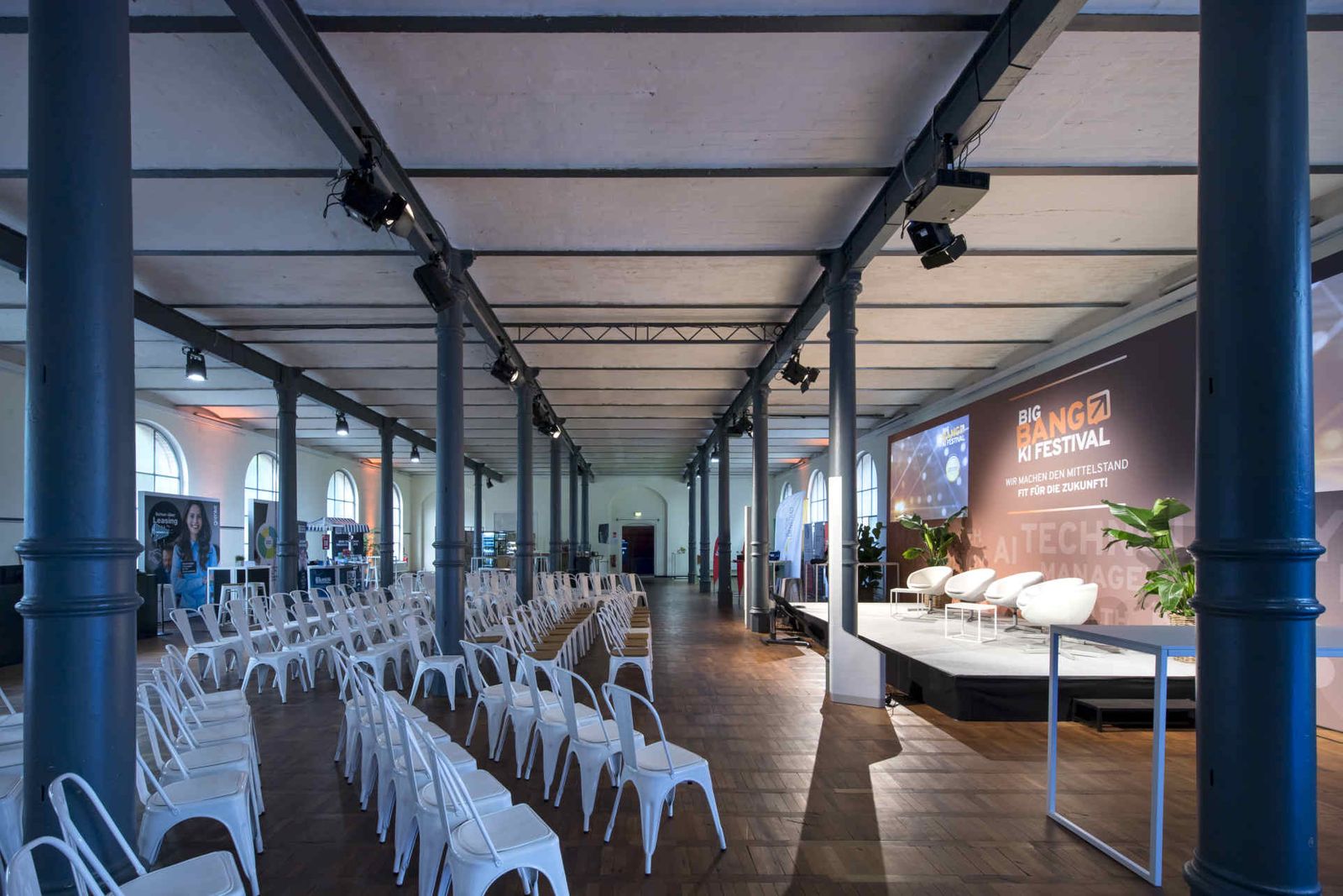 Großer Saal mit Reihenbestuhlung und einer Bühne mit großem Backdrop und Leinwänden