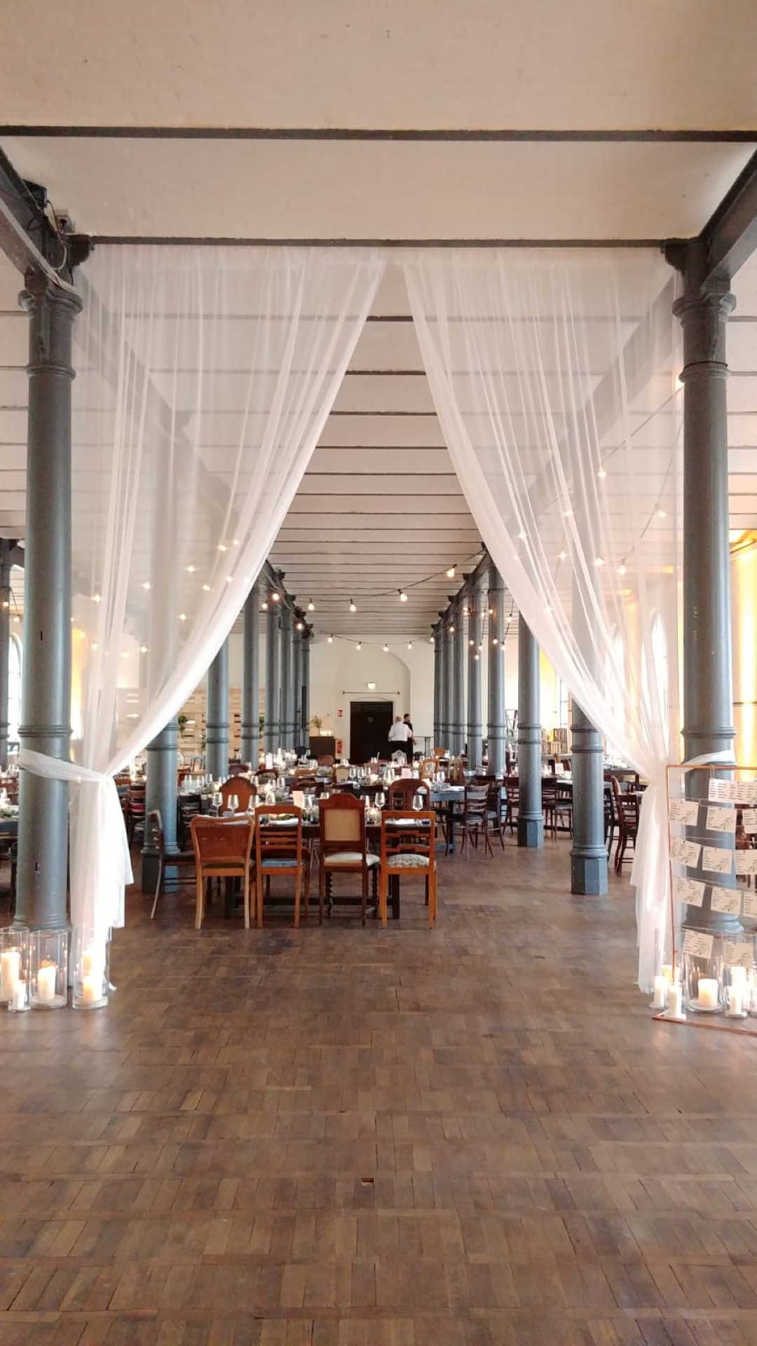 Saal mit festlich gedeckten Tischen und halbtransparentem Voile Vorhang.