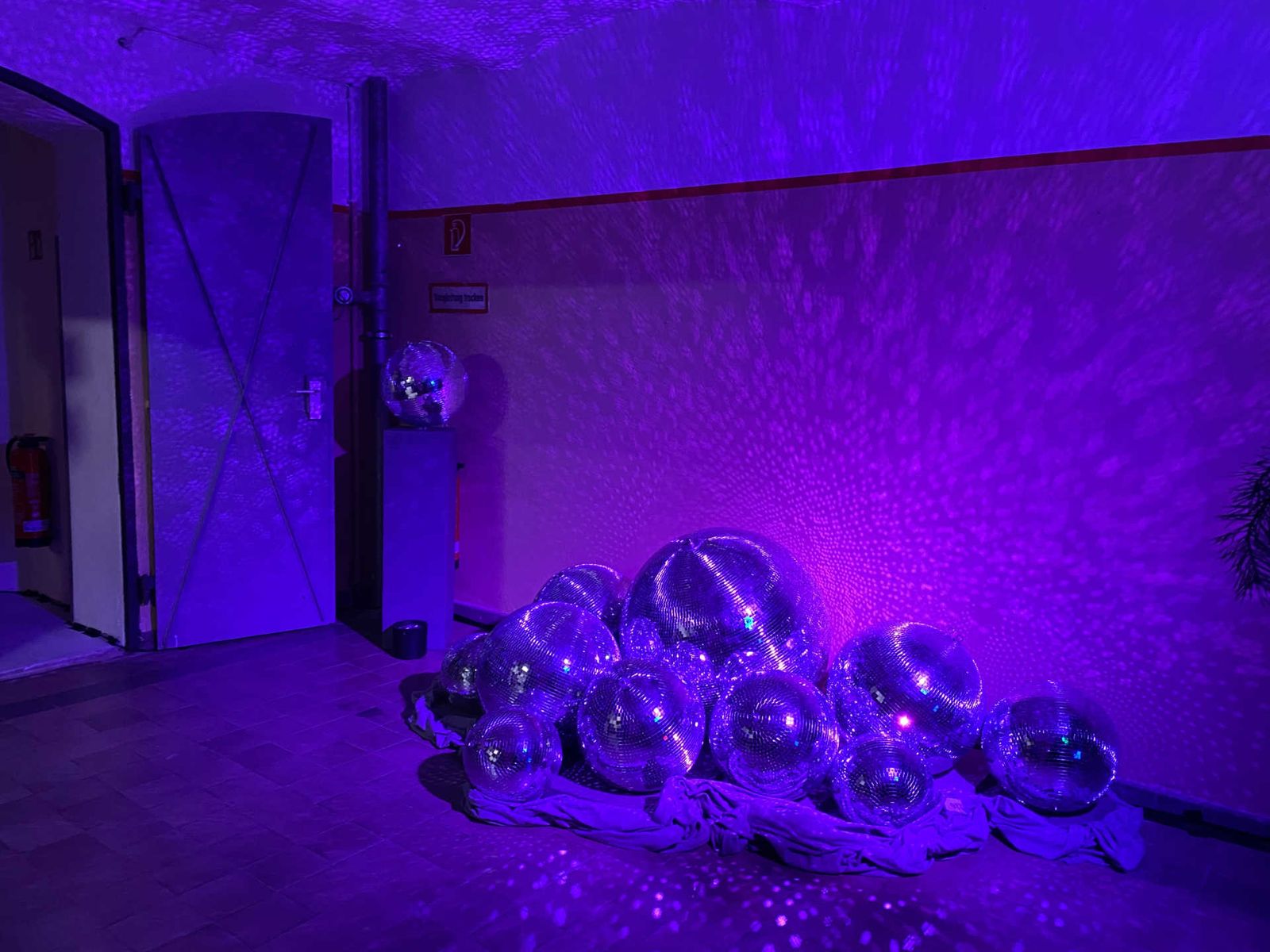 Room with a pile of disco balls on a cloth with purple lighting.