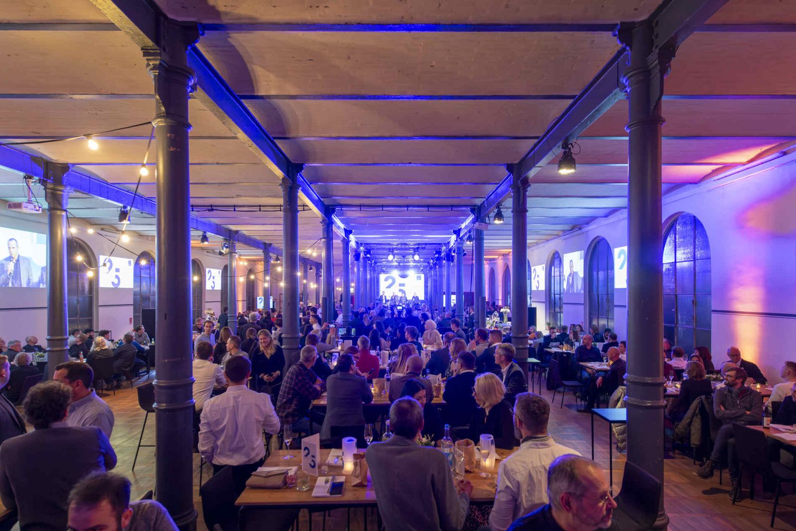 Eventsaal mit atmosphärischer Beleuchtung und Menschen während einer Veranstaltung.