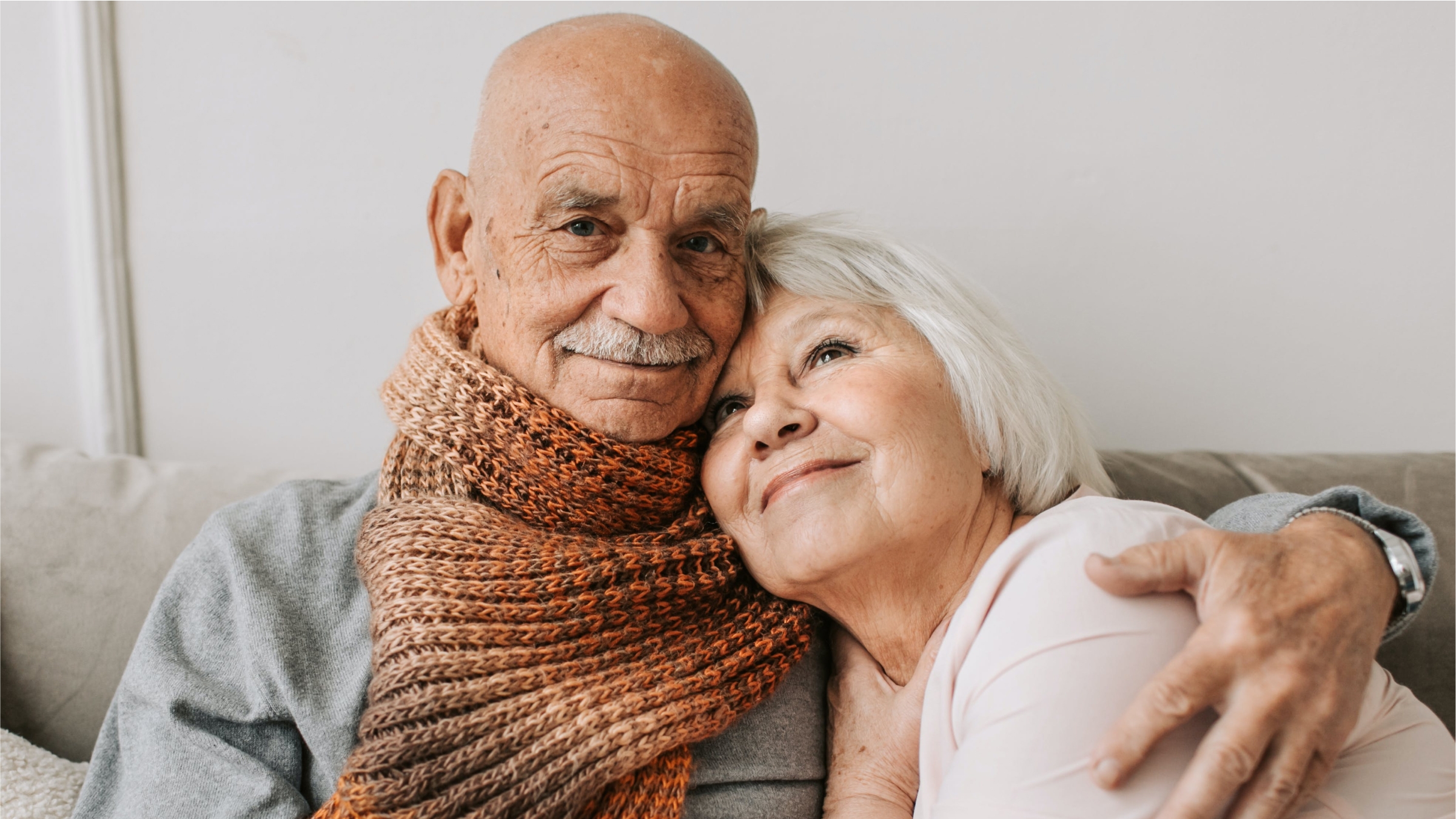 An older couple on a couch with the mans arm around the woman