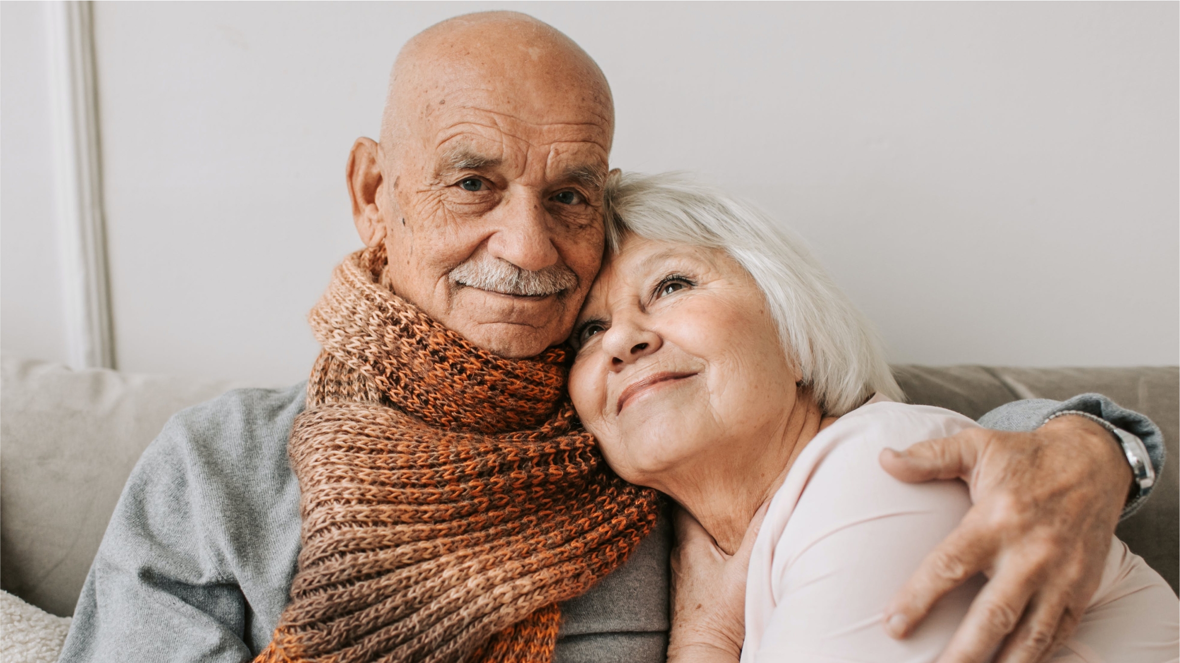 An older couple on a couch with the mans arm around the woman