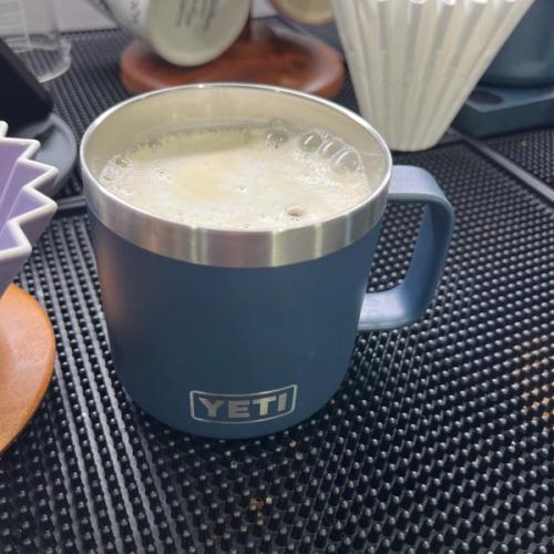 blue yeti mug containing coffee with white foam (from nitro cream) sitting ontop of a black bar mat amongst other coffee equipment