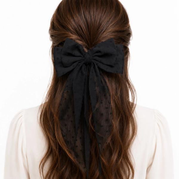 Back view of a woman wearing a large black sheer polka-dot fabric bow clip with long flowing tails in a half-up hairstyle.