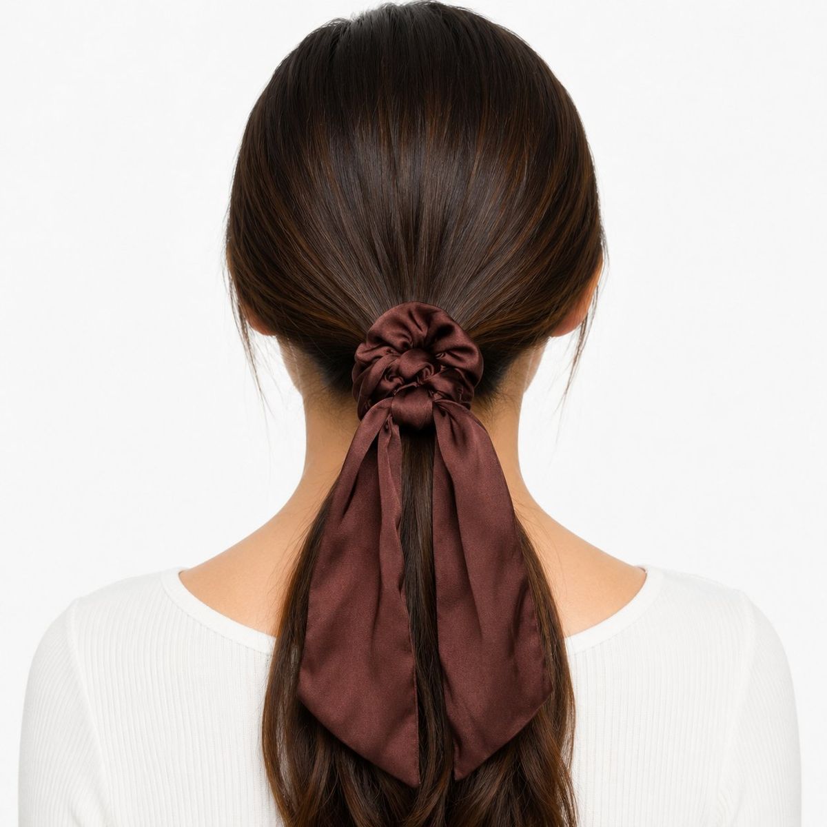 Back view of a woman with dark hair in a low ponytail secured by a chocolate brown satin scarf scrunchie with two long flowing ribbon tails.
