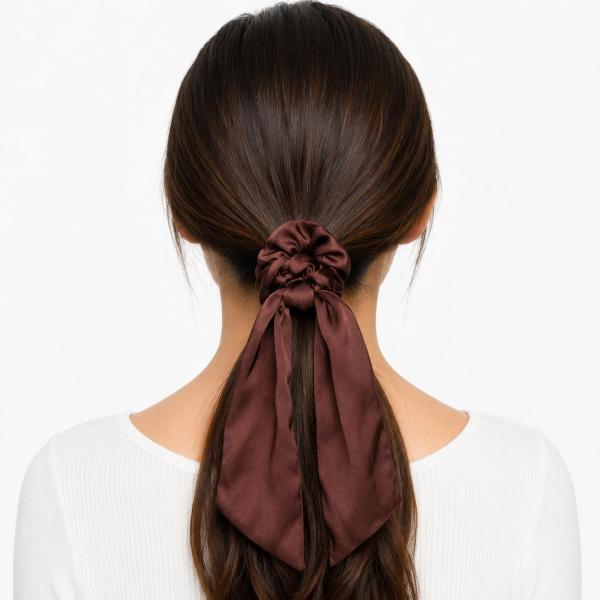 Back view of a woman with dark hair in a low ponytail secured by a chocolate brown satin scarf scrunchie with two long flowing ribbon tails.