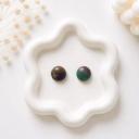 A pair of small round stud earrings with a marbled teal, purple, and brown pattern displayed on a white flower-shaped tray.