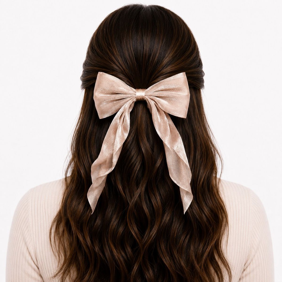 Back view of a woman with long wavy dark hair wearing a large oversized champagne shimmer bow clip with flowing ribbon tails in a half-up hairstyle.