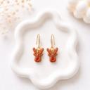 A pair of brown clay reindeer face dangle earrings with red noses on gold-tone crystal hook wires, displayed on a white wavy ceramic tray.