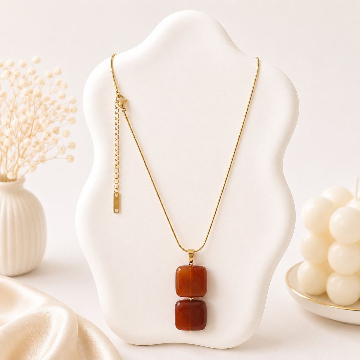 A gold snake chain necklace with two stacked square terracotta red stone pendants displayed on a white jewelry bust.