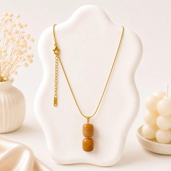A gold snake chain necklace with two stacked amber-colored barrel-shaped beads displayed on a white bust stand.
