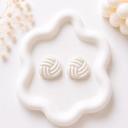 A pair of round white pearlescent clay stud earrings with a woven knot texture, displayed on a white wavy tray.