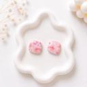 A pair of rounded square stud earrings with a pink and peach floral pattern displayed on a white wavy ceramic tray.