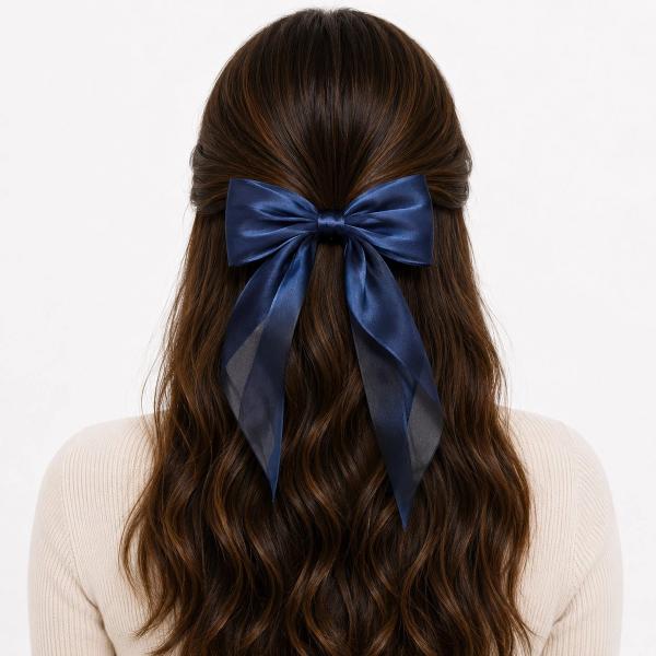 Back view of a woman with long wavy brown hair wearing a large navy blue satin bow clip with trailing ribbon tails in a half-up hairstyle.