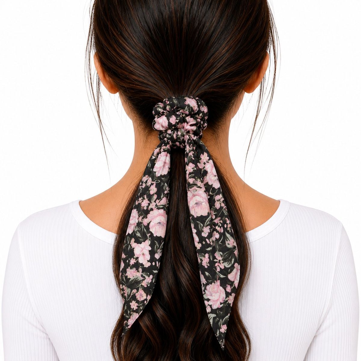 Back view of a woman wearing a black floral fabric scarf scrunchie with pink roses and long trailing tails in a low ponytail.