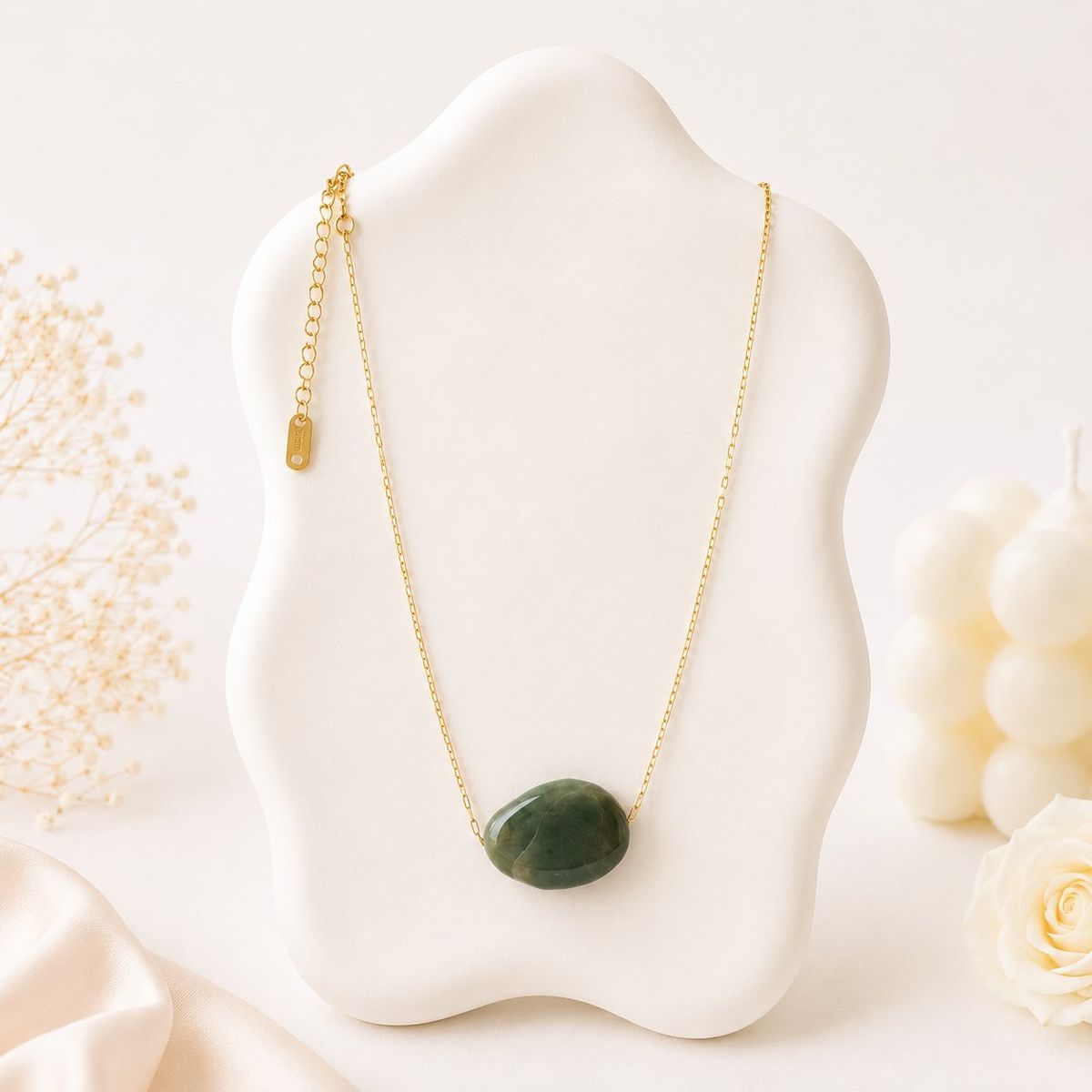 A smooth oval dark green stone pendant on a thin gold-tone chain displayed on a white sculptural jewelry bust.