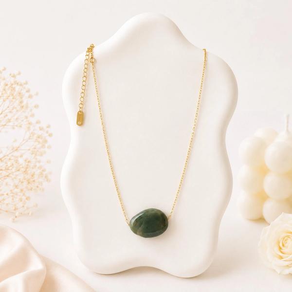 A smooth oval dark green stone pendant on a thin gold-tone chain displayed on a white sculptural jewelry bust.
