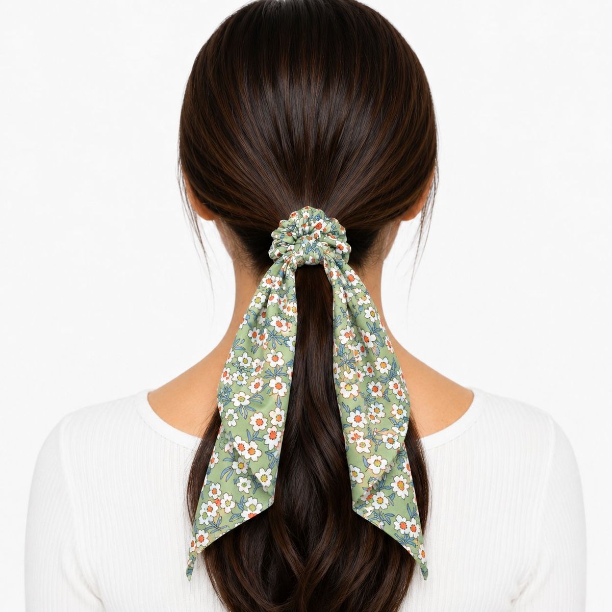 Back view of a woman wearing a sage green floral scarf scrunchie with long flowing tails holding a low ponytail.