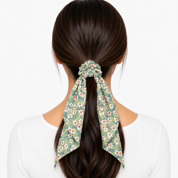 Back view of a woman wearing a sage green floral scarf scrunchie with long flowing tails holding a low ponytail.