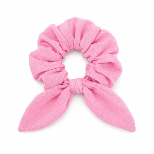 A bright pink fabric scrunchie with a knotted bow tie detail, laid flat on a white background.