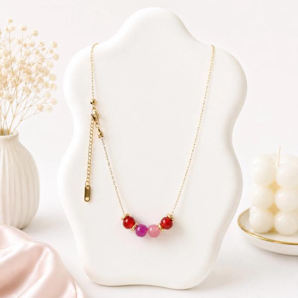 A gold-tone chain necklace with four round red, magenta, and pink beads centered on a white jewelry bust display.