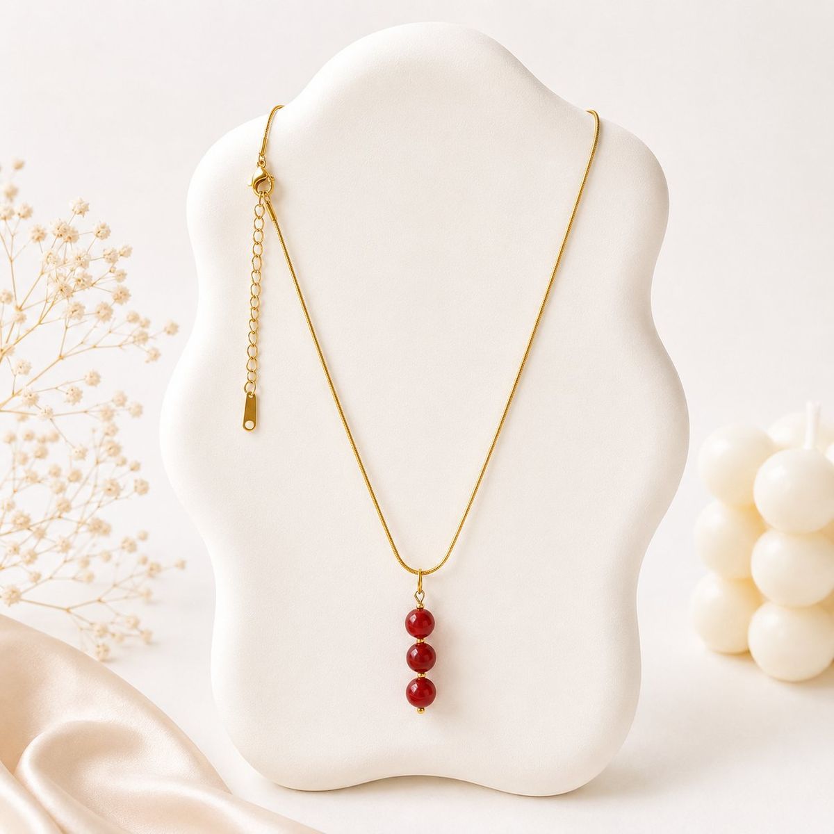 A gold snake chain necklace with three graduating deep red round bead pendants displayed on a white jewelry bust.