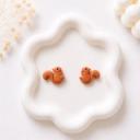 A pair of small terracotta brown clay squirrel stud earrings displayed on a white ceramic tray.